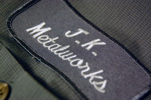 A stitched patch that reads JK Metalworks. It is on a work shirt.